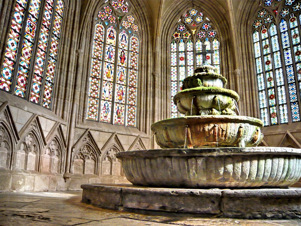 Ein alter Brunnen in einem gotischen Gebäude mit bunten Glasfenstern.