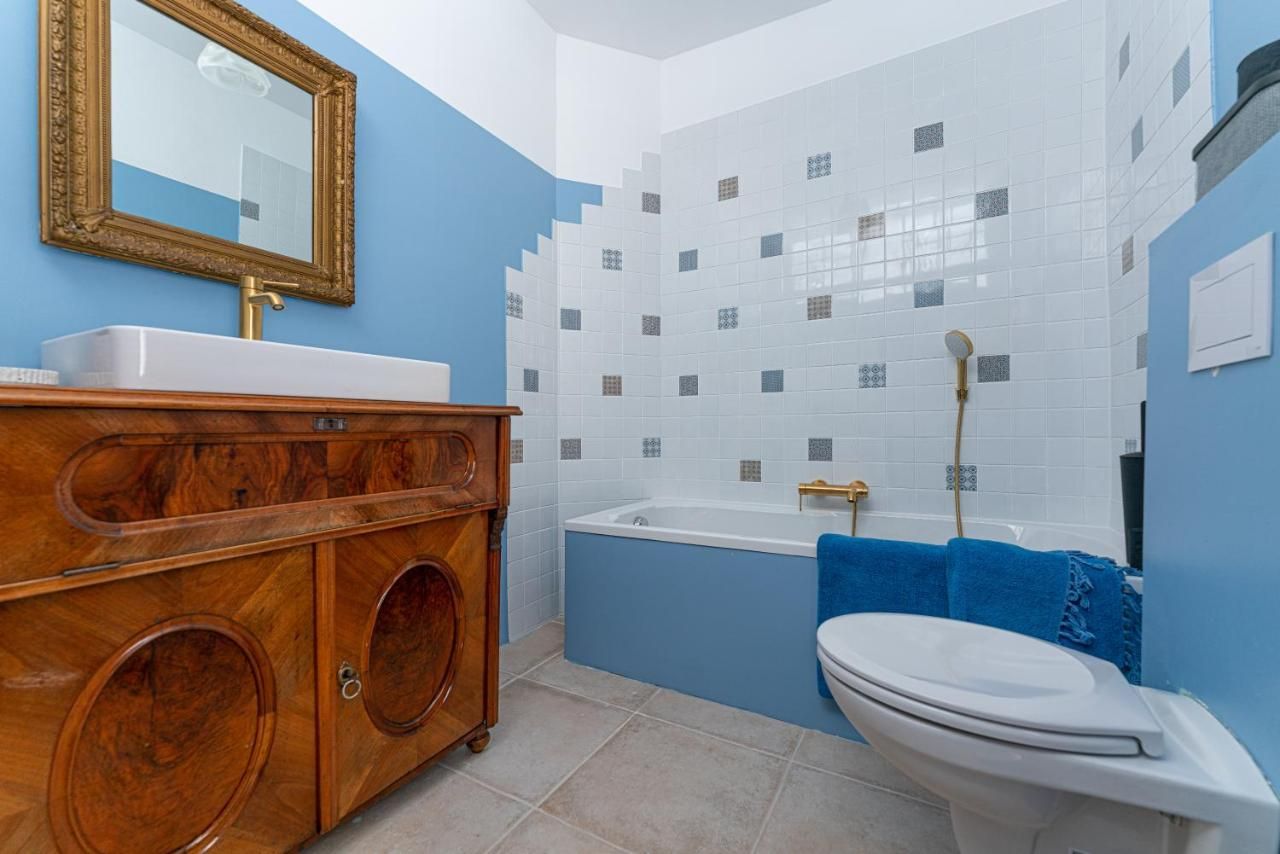 Ein Badezimmer mit blauen Wänden, einer Badewanne, einem Waschbecken auf einem Holzschrank und einem goldenen Spiegel.