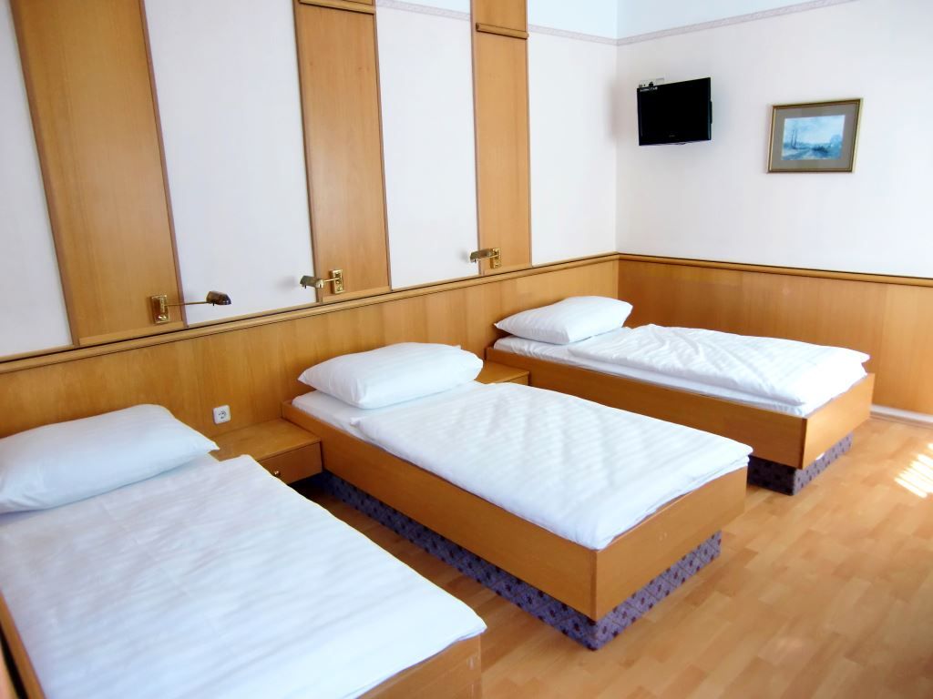Dreibettzimmer mit drei Einzelbetten, Holzwänden, Fernseher und Bild an der Wand.