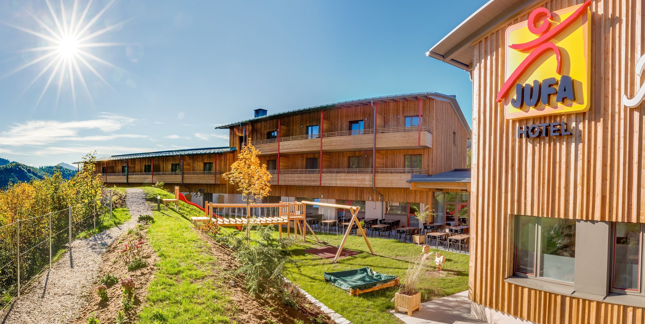 JUFA Hotel Annaberg mit Spielplatz und sonnigem Himmel.