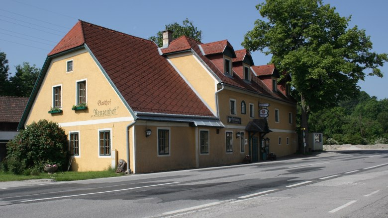 Gelbes Gasthaus mit rotem Dach an einer Stra&szlig;e, umgeben von B&auml;umen.