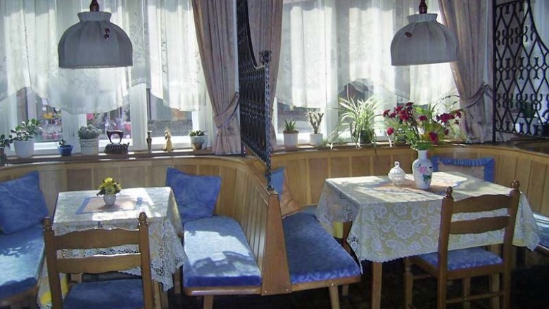 Gemütlicher Frühstücksraum mit Holzmöbeln und blauen Polstern, dekoriert mit Pflanzen und Blumen.