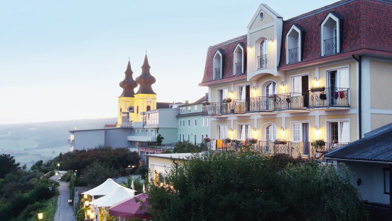 Ein Hotel mit Balkonen und einer Kirche im Hintergrund bei Dämmerung.