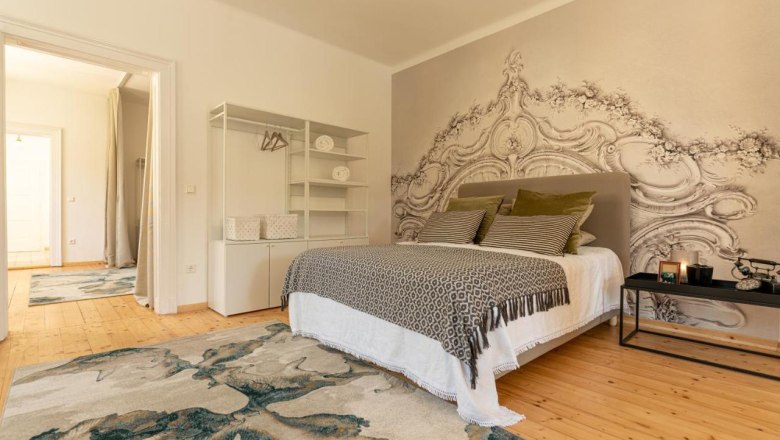 Ein stilvoll eingerichtetes Schlafzimmer mit einem großen Bett, dekorativen Kissen, einem Teppich und einer kunstvollen Wandgestaltung.
