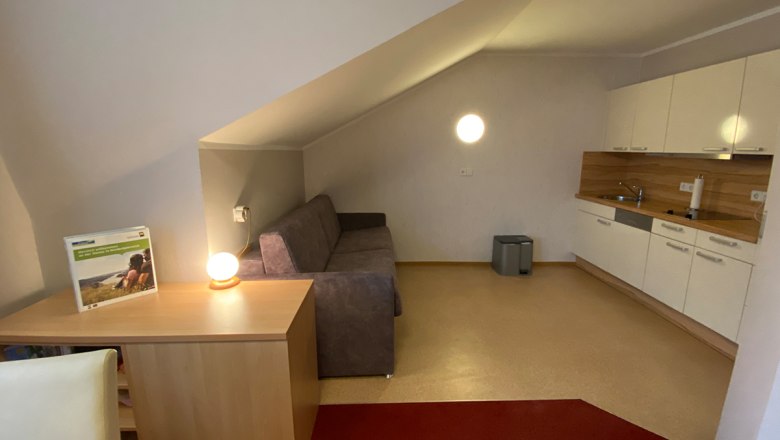 Innenansicht einer Ferienwohnung mit Sofa, Tischlampe und K&uuml;chenzeile.