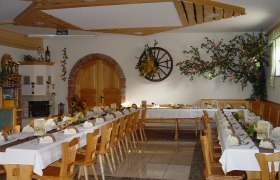 Ein festlich gedeckter Gastraum mit langen Tischen, dekoriert mit Blumen und Servietten, in einem rustikalen Ambiente.