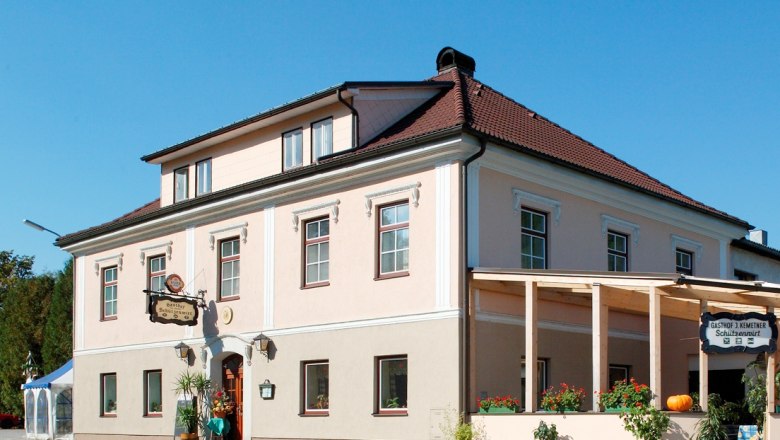 Ein traditionelles Gasthaus mit rosa Fassade und rotem Dach, dekoriert mit Pflanzen und einem Kürbis.