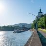 Fluss mit Schiff und Gebäude am Ufer, sonniger Himmel.