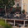 Gemütliche Terrasse eines Cafés mit Holztischen und Stühlen, umgeben von Pflanzen.