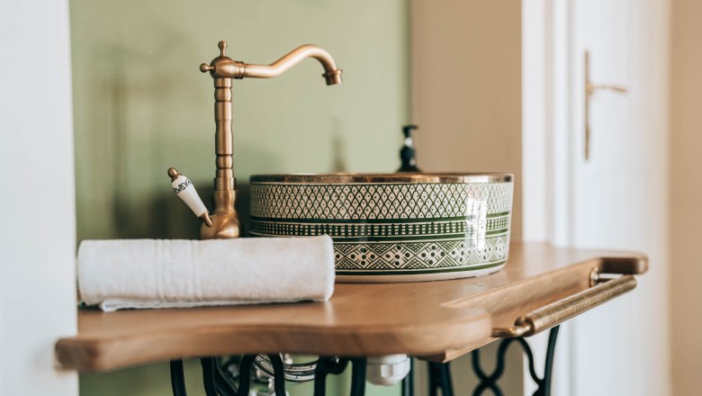Ein stilvolles Badezimmer mit einem dekorativen Waschbecken und einem goldenen Wasserhahn auf einem Holzwaschtisch.