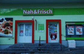 Eingang eines Nah&Frisch-Ladens mit Werbeplakaten und Schaufenster.
