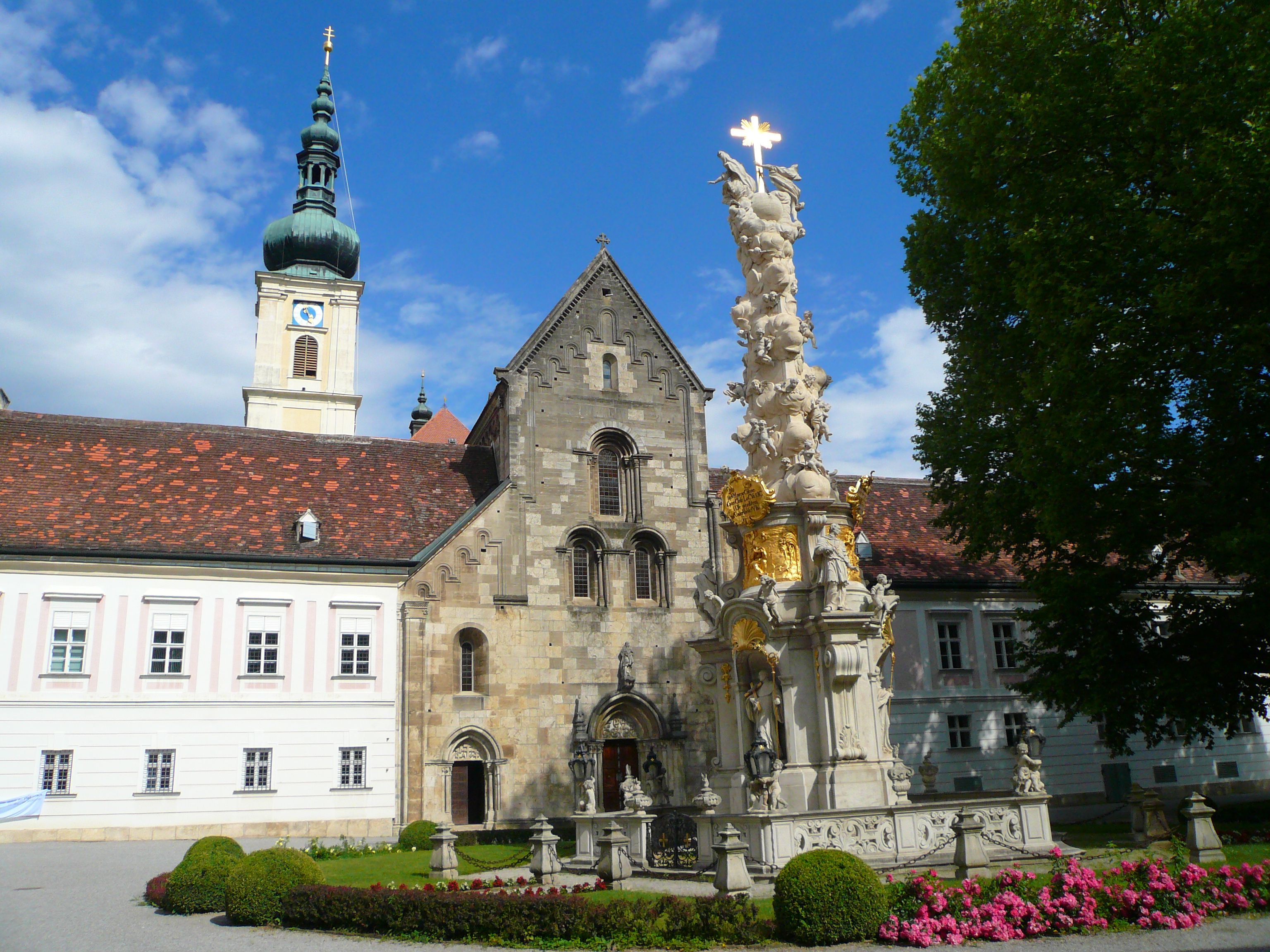Innenhof des Stifts Heiligenkreuz mit barocker Säule und Kirchturm.