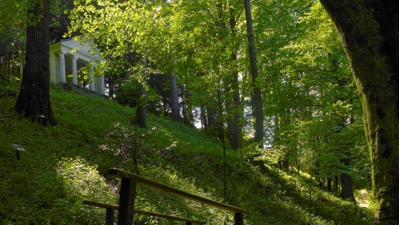 Ein kleiner Tempel im Stiftspark Lilienfeld, umgeben von dichtem Wald und grünem Laub.