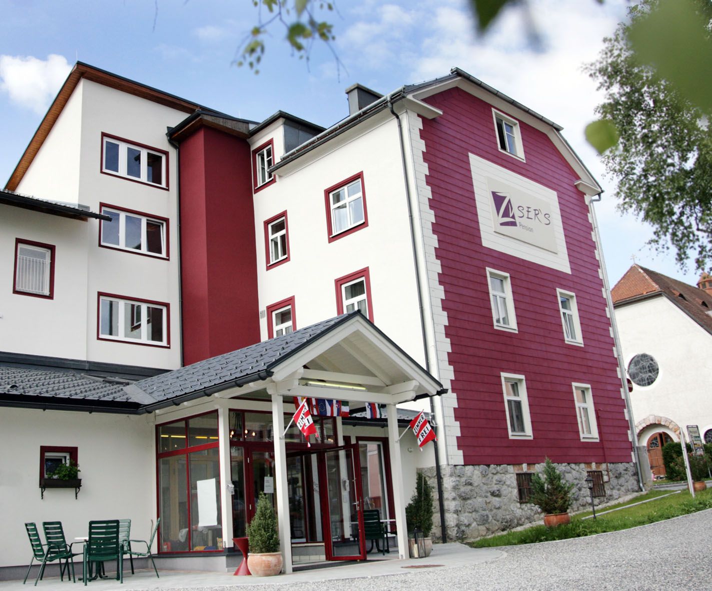 Außenansicht eines mehrstöckigen Gebäudes mit roter und weißer Fassade, beschriftet mit "Zusers Pension".