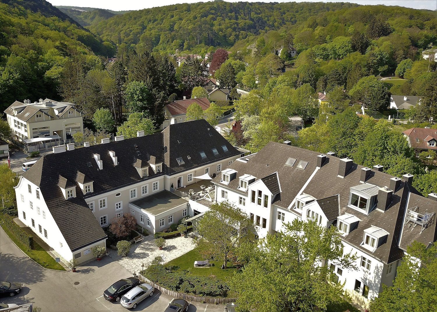 Luftaufnahme eines großen Gebäudekomplexes umgeben von grünen Bäumen und Hügeln.