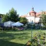 Garten mit Blumenbeeten, weißen Zelten und historischem Gebäude im Hintergrund.