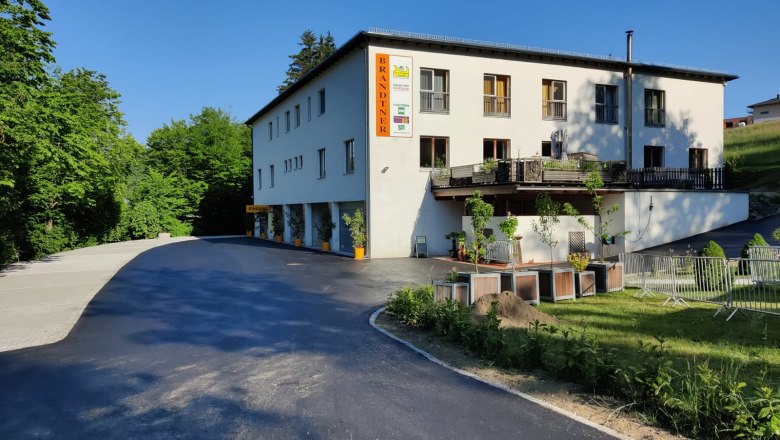 Brandtner Seminar & Komfortzimmer, © Brandtner Gebäude mit der Aufschrift 'Brandtner', umgeben von Bäumen und einem Parkplatz.