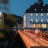 Ein Paar spaziert abends über eine beleuchtete Brücke vor einem Hotel.