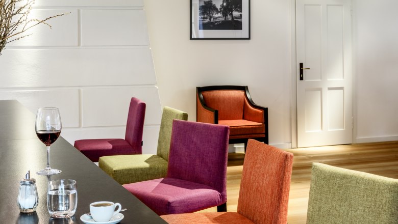 Innenansicht eines modernen Hotel-Lounges mit bunten Stühlen, einem Tisch mit Getränken und einem Bild an der Wand.