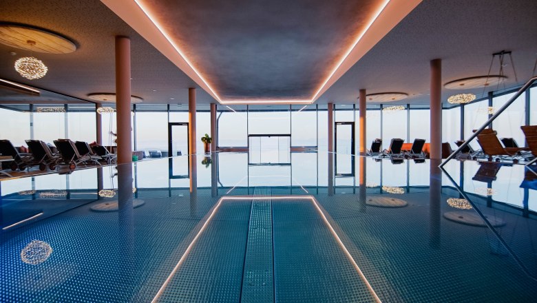 Infinitypool innen, © Hotel Schachner_MIKU Media Innenansicht eines Infinitypools mit Liegestühlen und großen Fenstern.