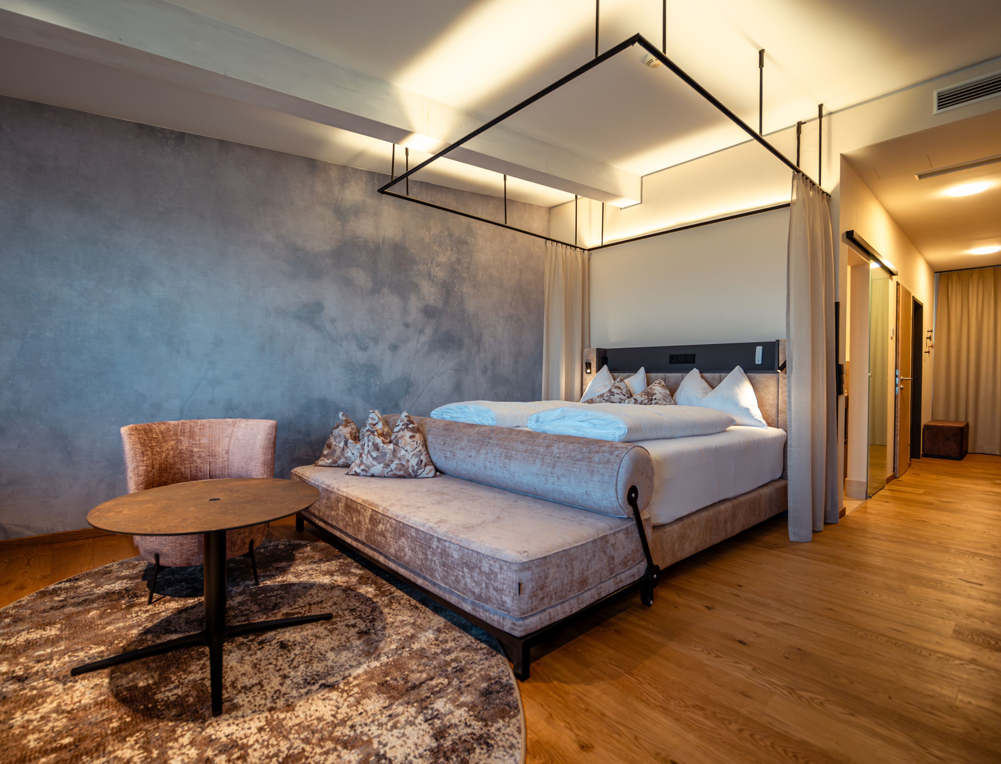 Modernes Hotelzimmer mit Himmelbett, Sessel und Tisch auf Holzboden.