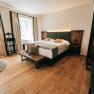 Modern eingerichtetes Hotelzimmer mit Doppelbett, Holzboden und großen Fenstern.