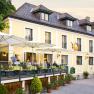 Ein gelber Landgasthof mit Terrasse und Sonnenschirmen, auf der Menschen sitzen.