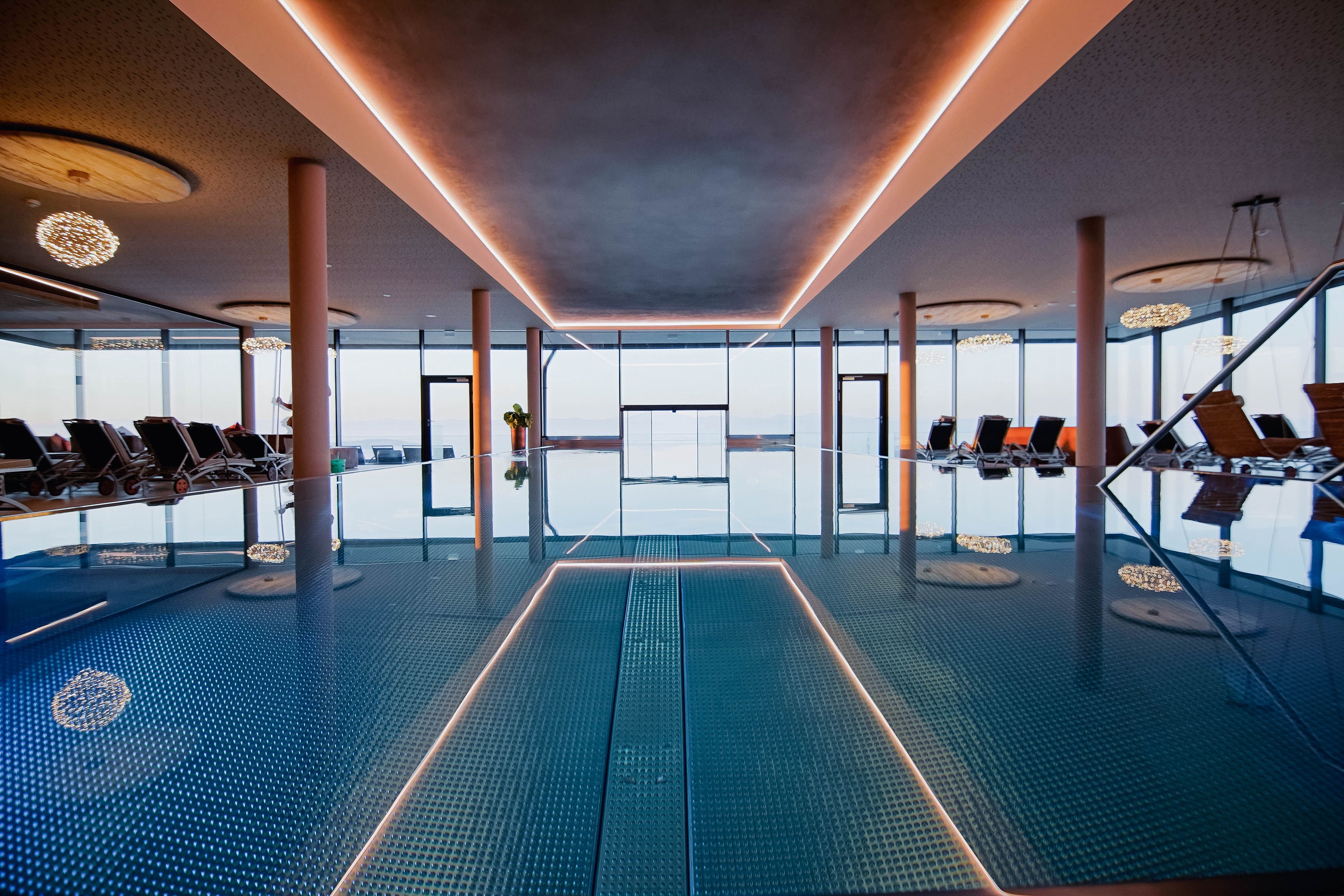 Innenansicht eines Infinitypools mit Liegestühlen und großen Fenstern.