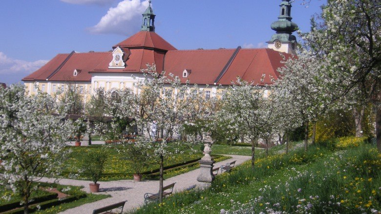 Historischer Hofgarten mit blühenden Bäumen und einem großen Gebäude im Hintergrund.