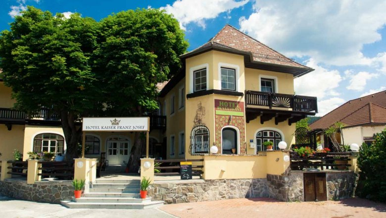 Eingang des Hotel Kaiser Franz Josef mit gelber Fassade und Balkon.