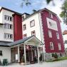 Außenansicht eines mehrstöckigen Gebäudes mit roter und weißer Fassade, beschriftet mit "Zusers Pension".