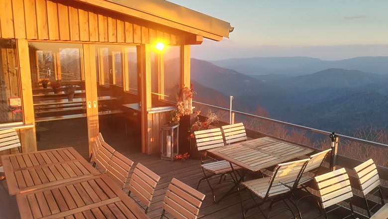 Terrasse mit Holzmöbeln und Bergblick bei Sonnenuntergang.