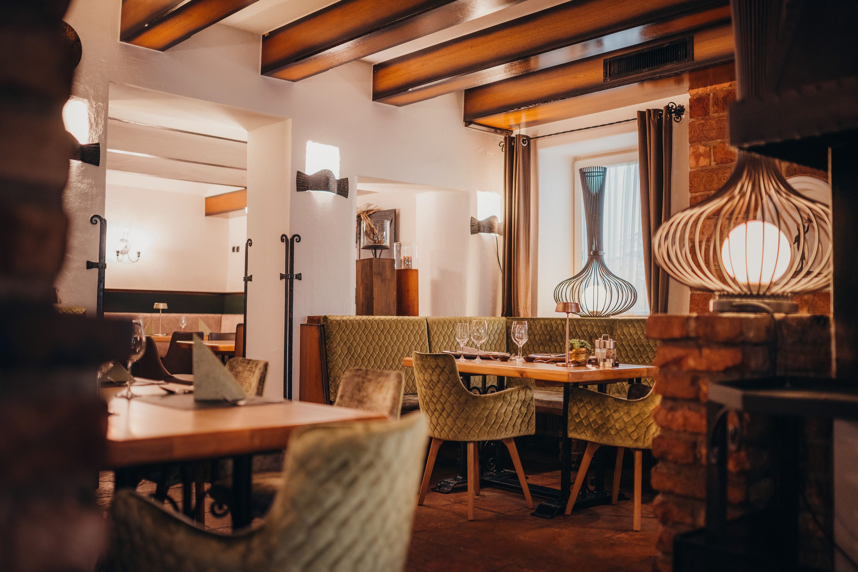 Gemütliches Restaurant mit Holzbalken, grünen Polsterstühlen und dekorativen Lampen.