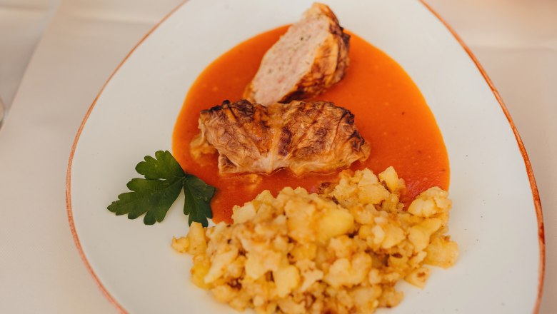 Krautroulade mit Kartoffeln und Soße auf weißem Teller serviert.