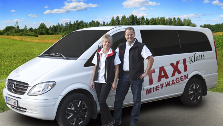 Zwei Personen stehen vor einem weißen Mercedes-Van mit der Aufschrift 'Taxi Mietwagen Klaus' auf einer ländlichen Straße.