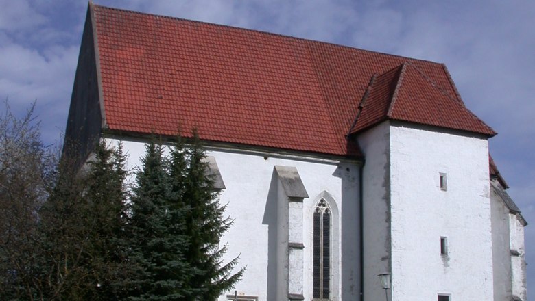 Andreaskirche in Kirchberg an der Pielach mit rotem Ziegeldach und weißer Fassade, umgeben von Bäumen und einem Weg im Vordergrund.