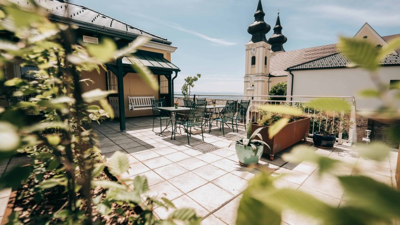 Terrasse mit Tisch und Stühlen, im Hintergrund Kirchturm mit zwei Türmen.