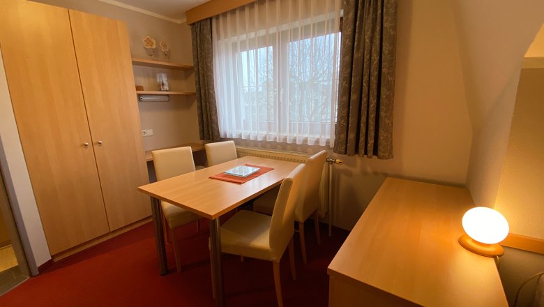 Ein gemütlicher Raum mit Holzmöbeln, Tisch, Stühlen und einem Fenster mit Vorhängen.