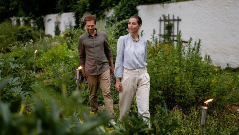 Ein Mann und eine Frau spazieren durch einen grünen Garten, umgeben von Pflanzen.