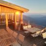 Terrasse mit Holzm&ouml;beln und Bergblick bei Sonnenuntergang.