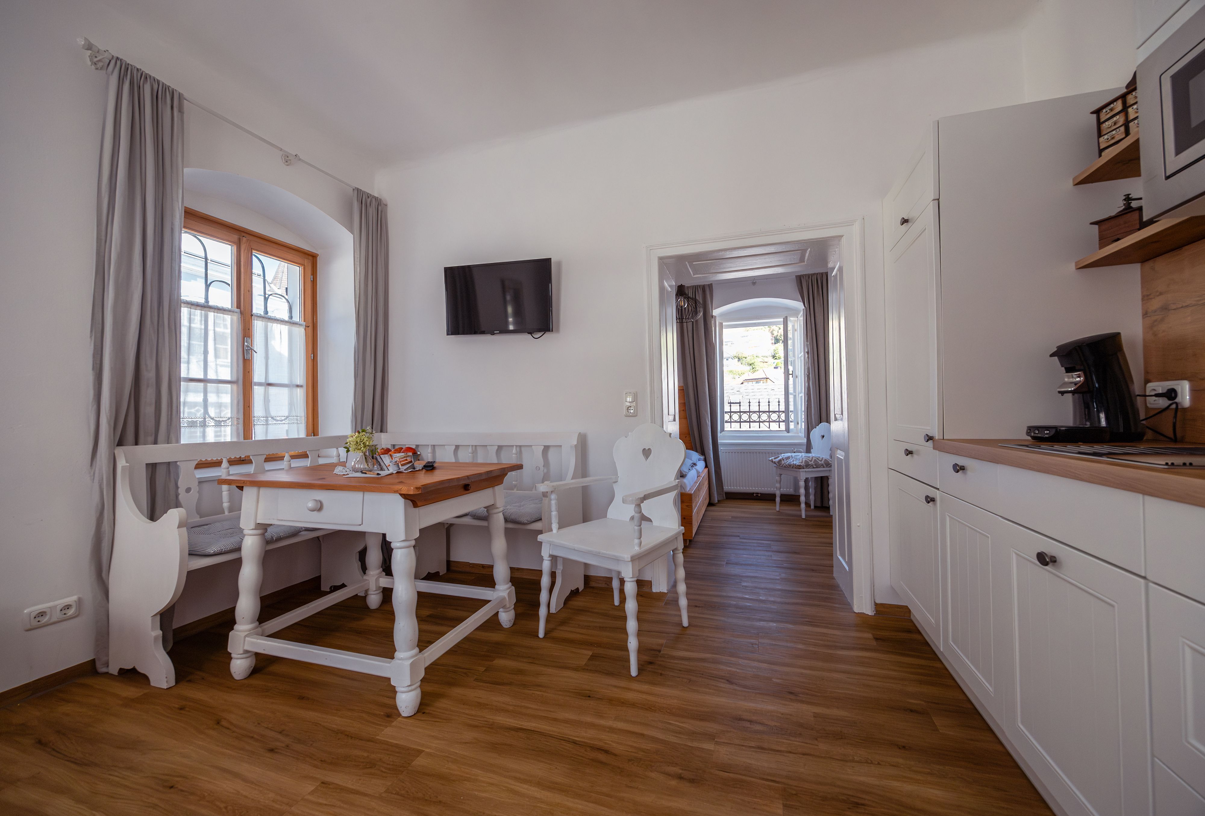 Helles, gemütliches Zimmer mit Holzboden, Esstisch, Stühlen und Küchenzeile.