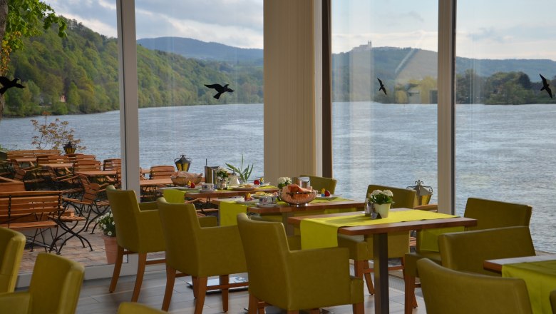 Innenansicht eines Restaurants mit Blick auf einen Fluss und grüne Hügel.