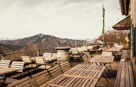 Leere Terrasse mit Holztischen und -stühlen, Berglandschaft im Hintergrund.