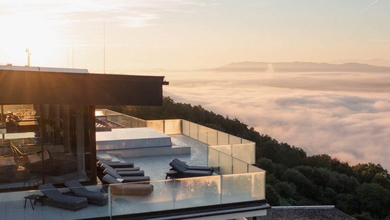Modernes Gebäude mit Terrasse über einem Nebelmeer bei Sonnenaufgang.