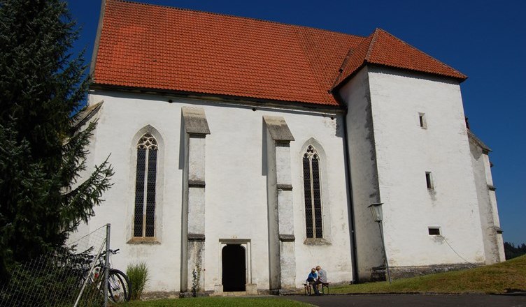 Wei&szlig;e Kirche mit rotem Dach und gotischen Fenstern, blauer Himmel.