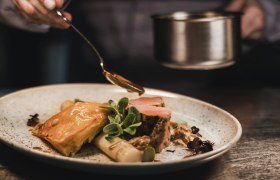 Ein Teller mit Kalbsmedaillons, Spargel und Blätterteig, garniert mit Sauce und Kräutern.