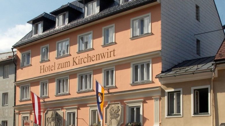 Fassade des Hotels zum Kirchenwirt mit Fahnen und blauer Himmel.