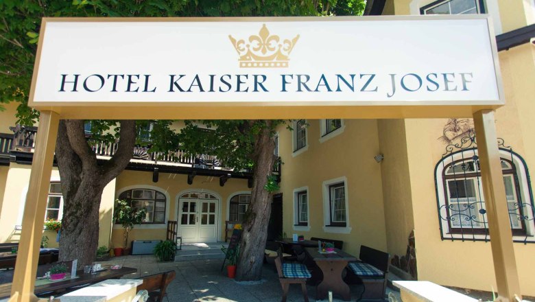 Eingang des Hotel Kaiser Franz Josef mit Schild und B&auml;umen.