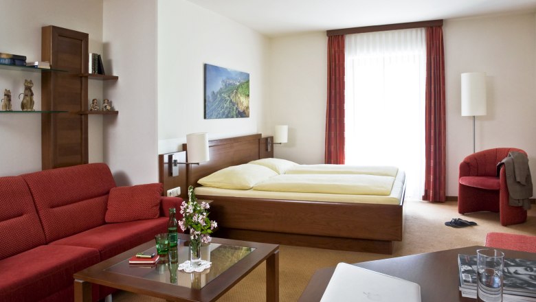 Gemütliches Hotelzimmer mit Doppelbett, rotem Sofa, Glastisch und Dekorationen.