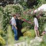 Drei Personen stehen in einem blühenden Garten und unterhalten sich.
